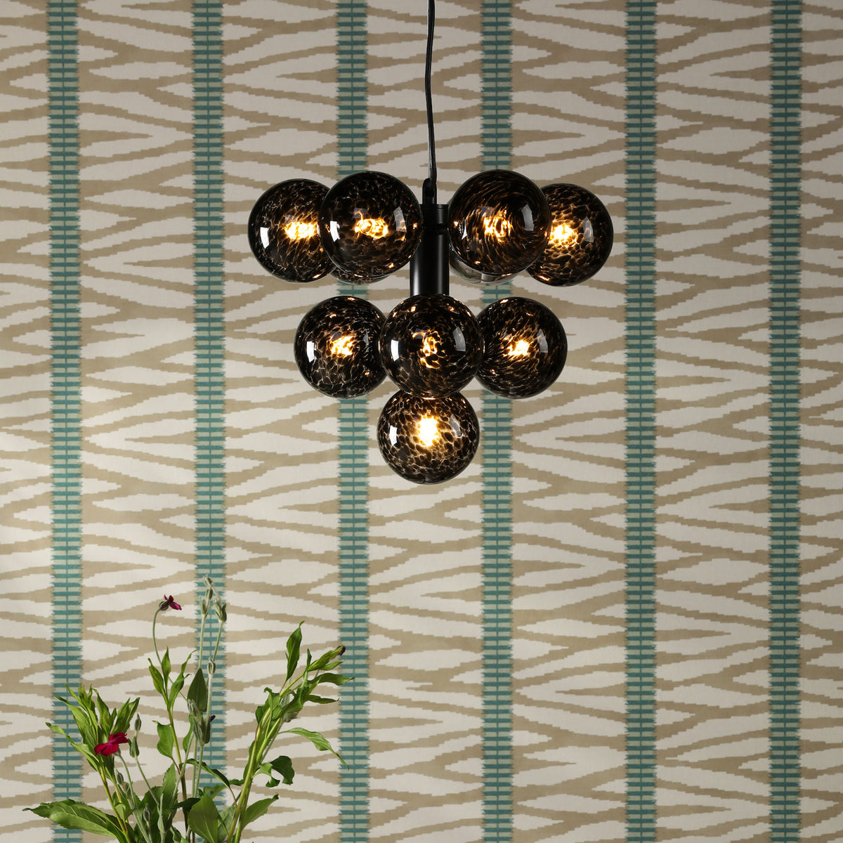 A black chandelier with seven round, textured glass globes hangs against a patterned wallpaper