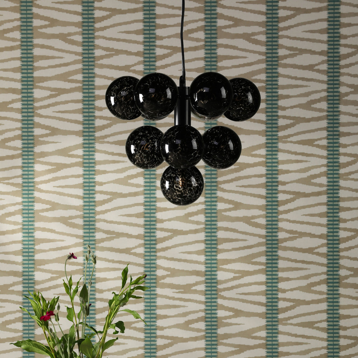 Black glass pendant light with seven globes against a patterned wallpaper