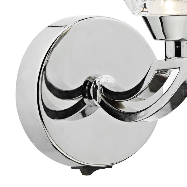 Close-up of a chrome wall sconce base with a curved arm and a small black switch at the bottom.