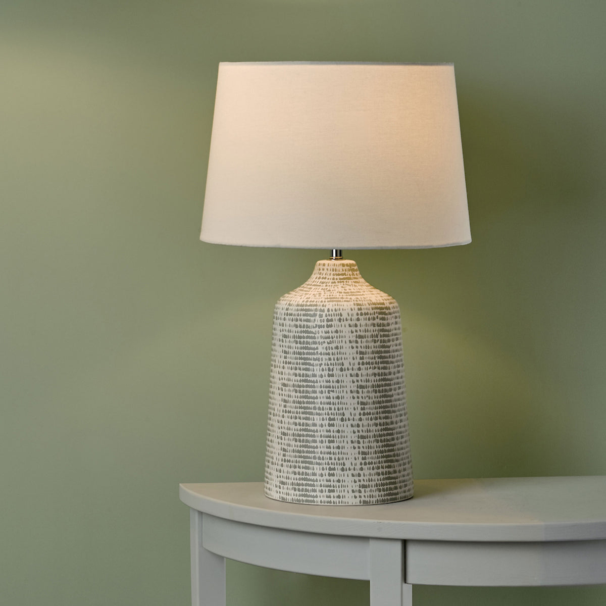 Table lamp with a textured gray base and a cream fabric shade on a light gray table.