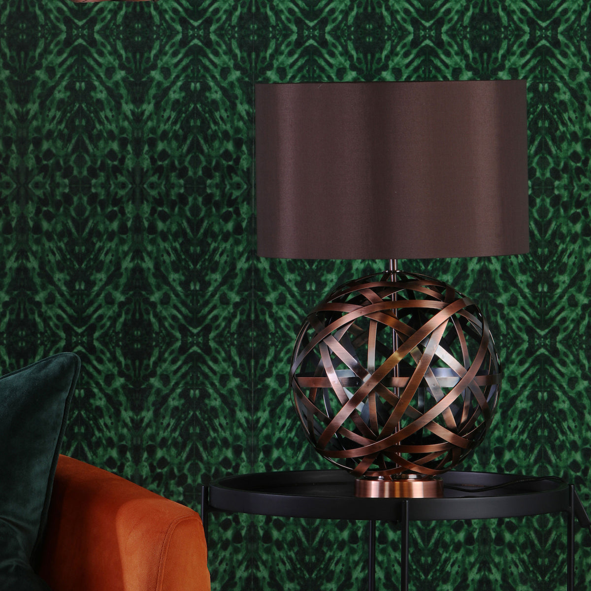 Table lamp with a brown shade and a copper-toned, spherical base on a black side table.