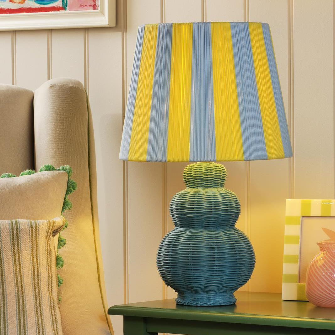 Table lamp with a blue and yellow striped shade and a blue tiered rattan base