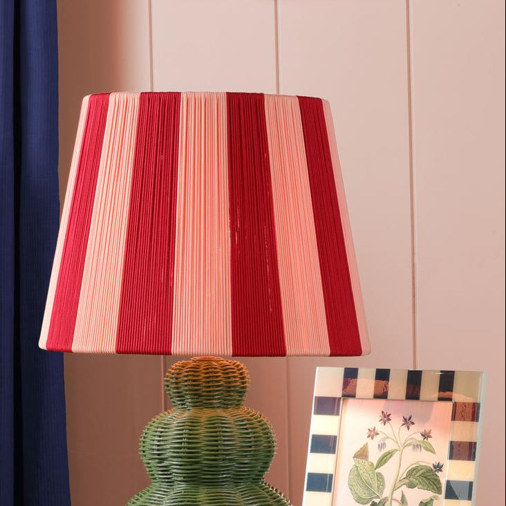 Table lamp with a red and pink striped pleated shade and a green tiered wicker base