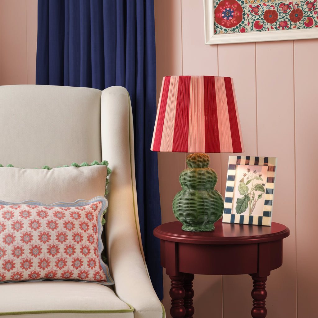 Joules Whitby table lamp in matt green with a striped red and pink fabric shade on a dark red side table