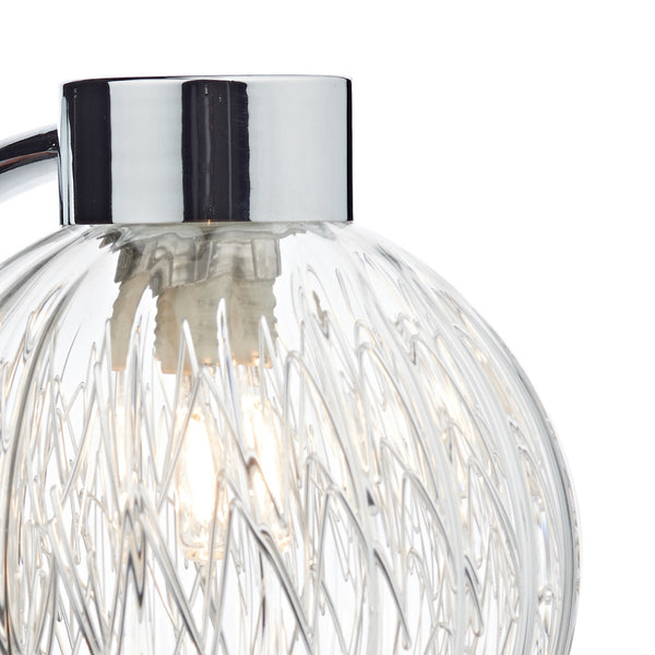 Close-up of a clear glass lamp shade with a textured, wavy pattern and a glowing bulb inside.