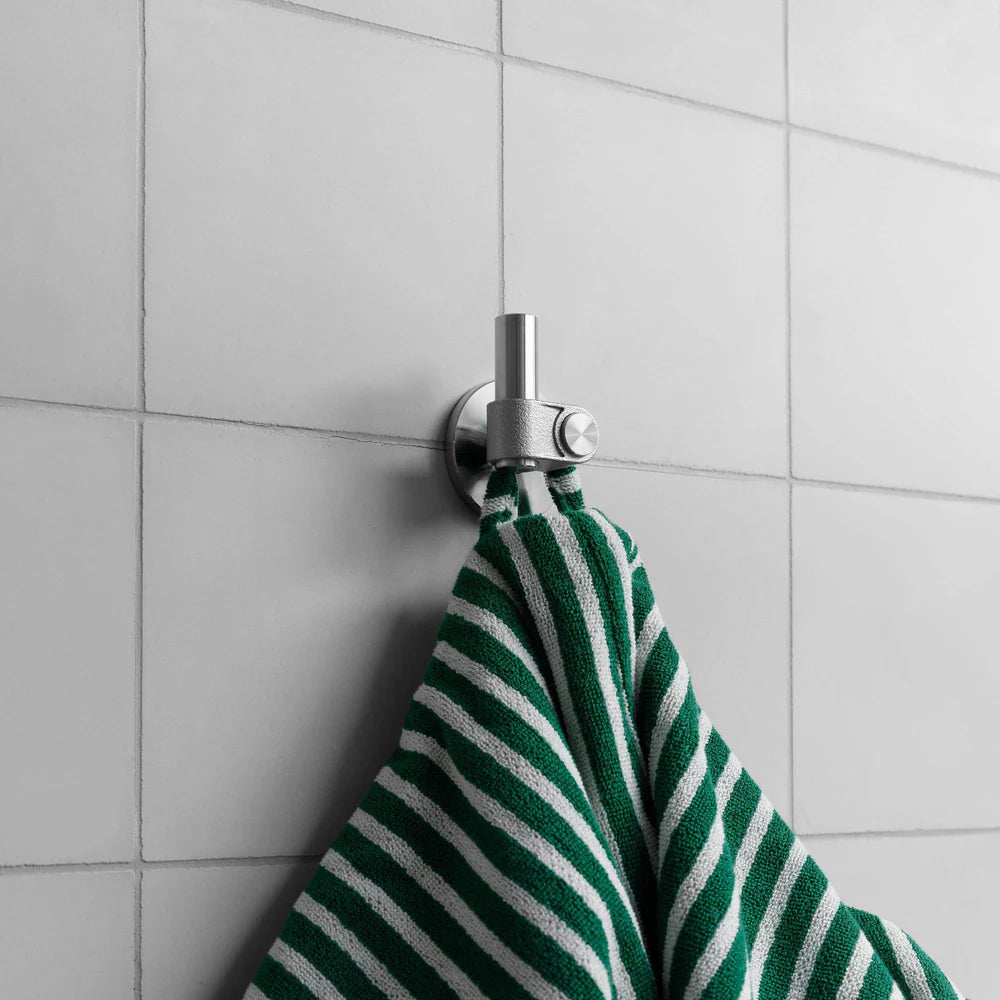 Green and white striped towel hanging on a silver hook against a tiled wall