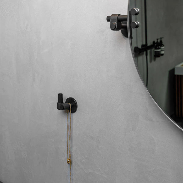 Black wall hook with a gold necklace hanging on it, next to a round mirror