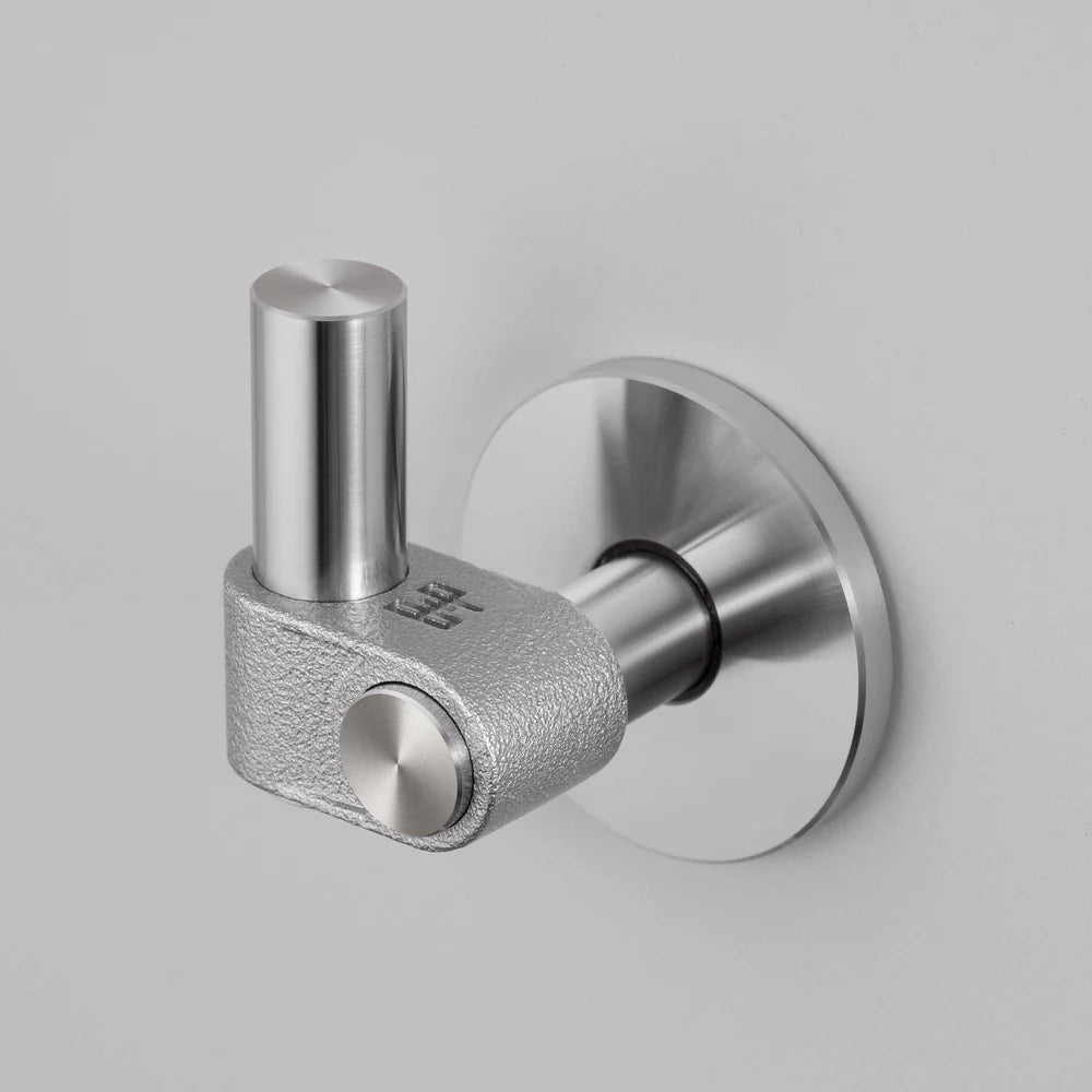 Close up of a silver wall hook with a textured base and smooth cylindrical arm, mounted on a light grey wall