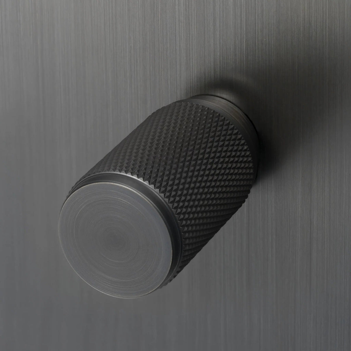 Close-up of a dark grey cylindrical knob with a textured diamond pattern on its side
