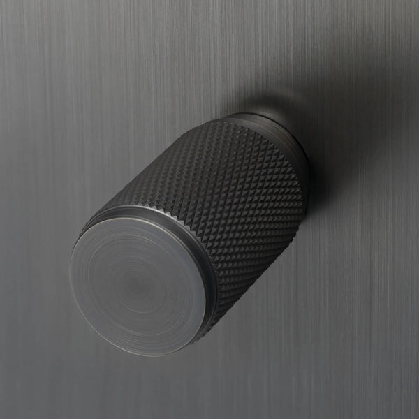 Close-up of a dark grey cylindrical knob with a textured diamond pattern on its side