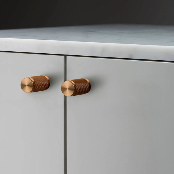 Two copper knurled cabinet handles on light grey cabinet doors