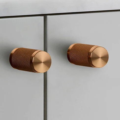 Two copper knurled cabinet knobs on light grey cabinet doors