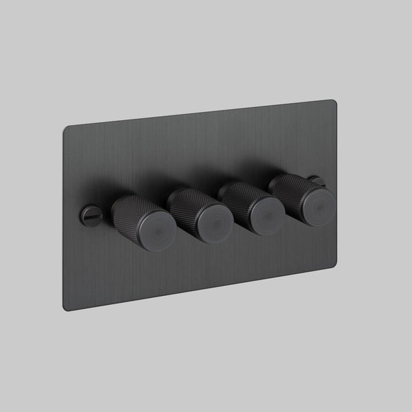 Four black knurled dimmer switches on a rectangular black faceplate with a visible screw on the left