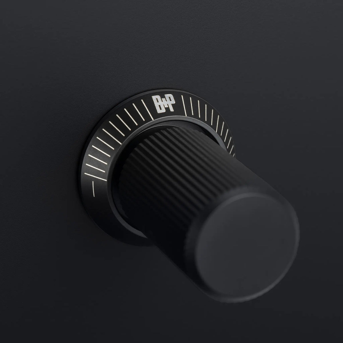 Close up of a black volume knob with the B&P logo and white markings on a black background