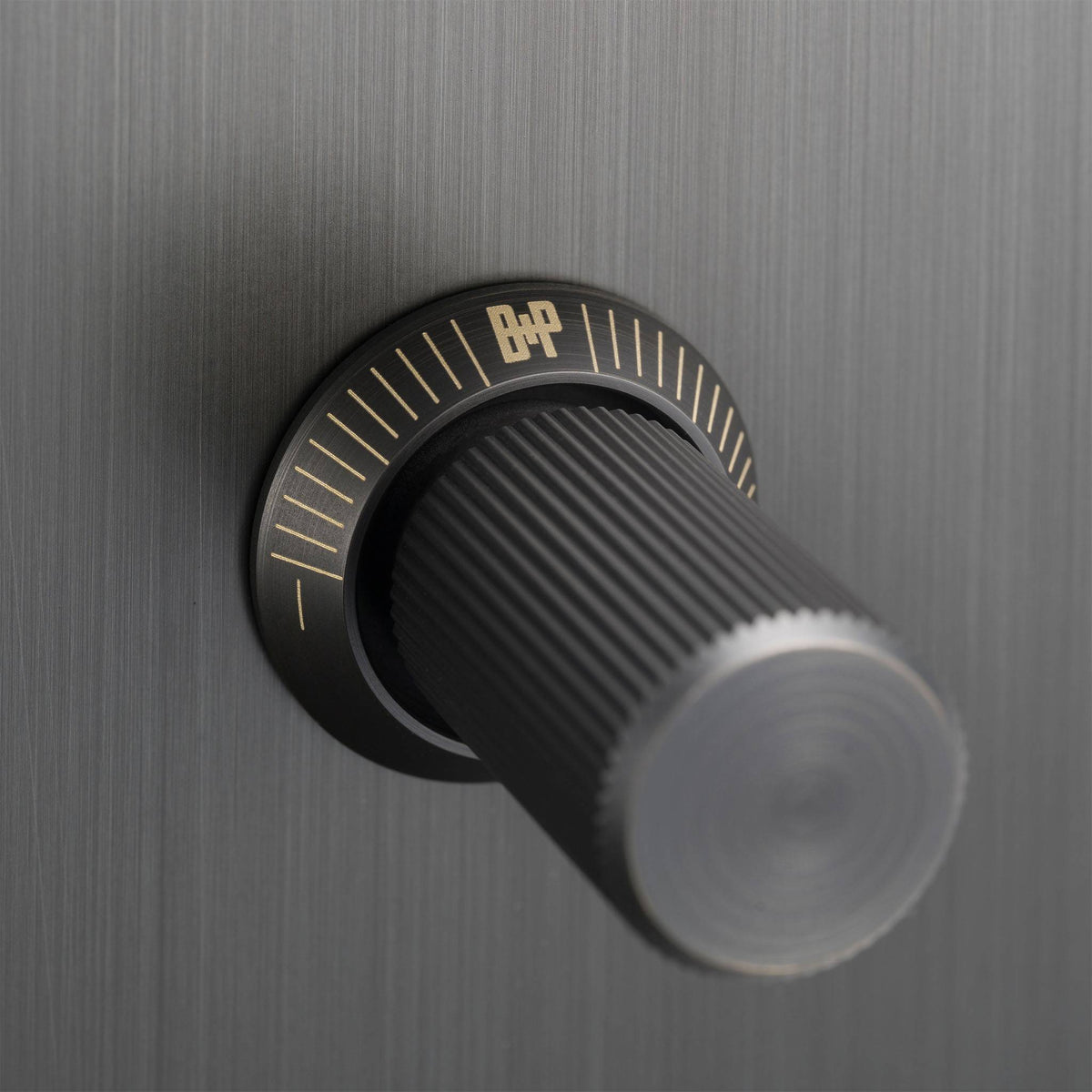 Close up of a black knob with gold markings on a brushed metal surface