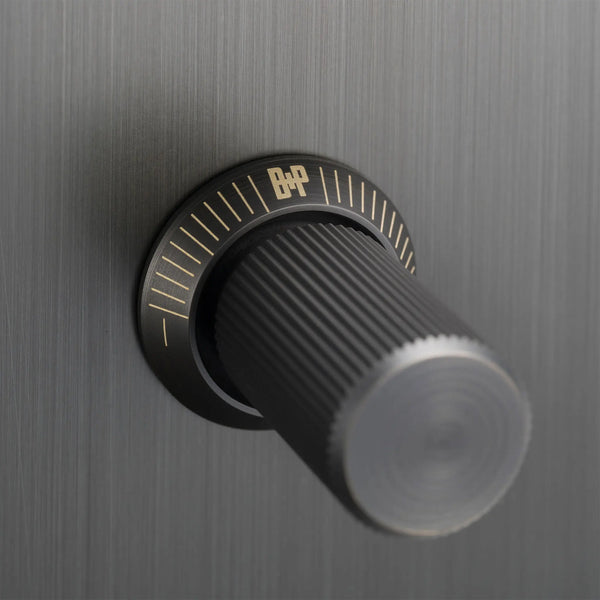 Close up of a black rotary knob with gold markings on a brushed dark grey surface