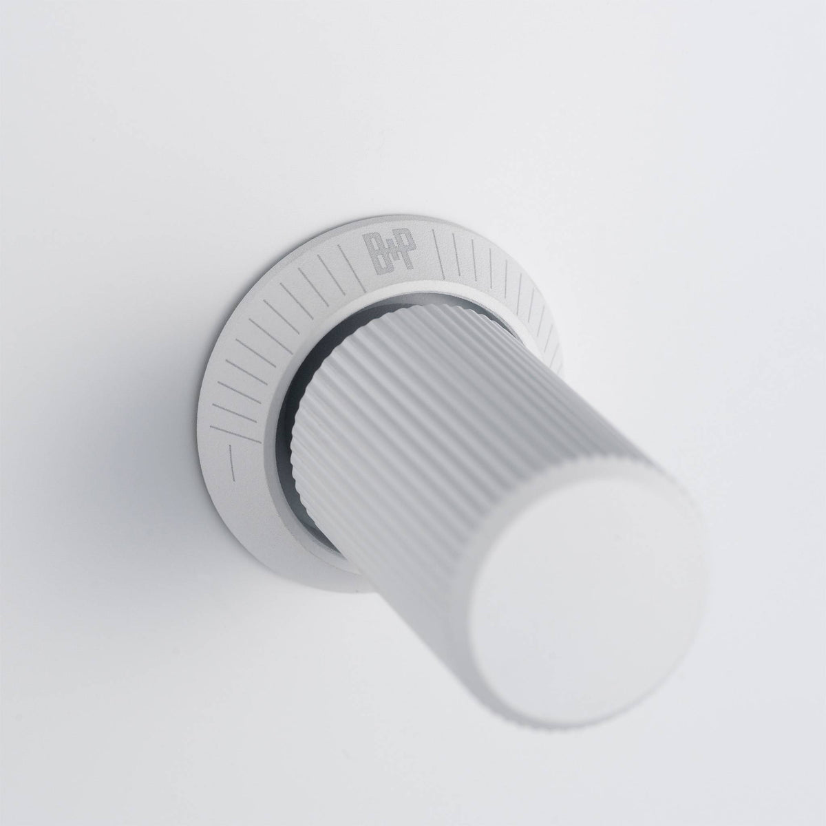 Close up of a white volume knob with the B&P logo on a white surface