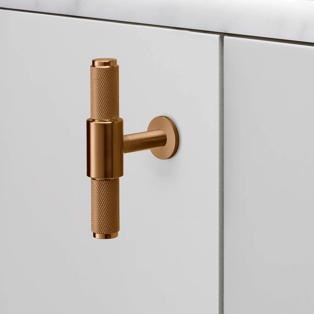 Knurled T-bar handle in bronze on a white cabinet
