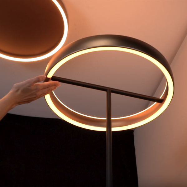 Hand adjusting a modern black floor lamp with a glowing circular LED light.