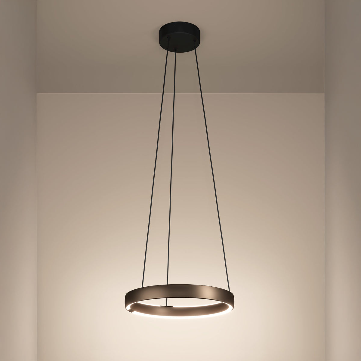 Modern circular pendant light with a bronze finish, emitting a warm glow, suspended from a black ceiling mount.