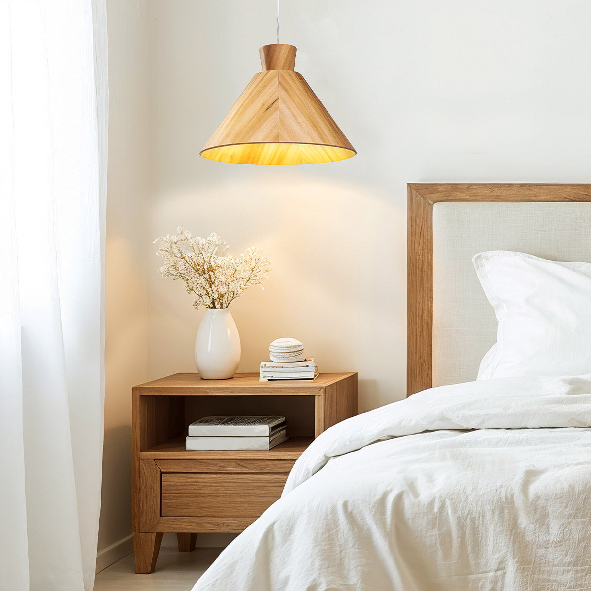 Wooden pendant light hanging above a bedside table with a white vase of flowers and books