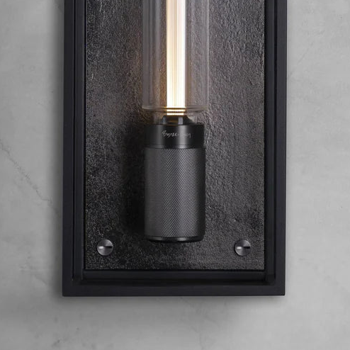 Close up of a black wall light with a textured base and a clear glass tube with a glowing bulb