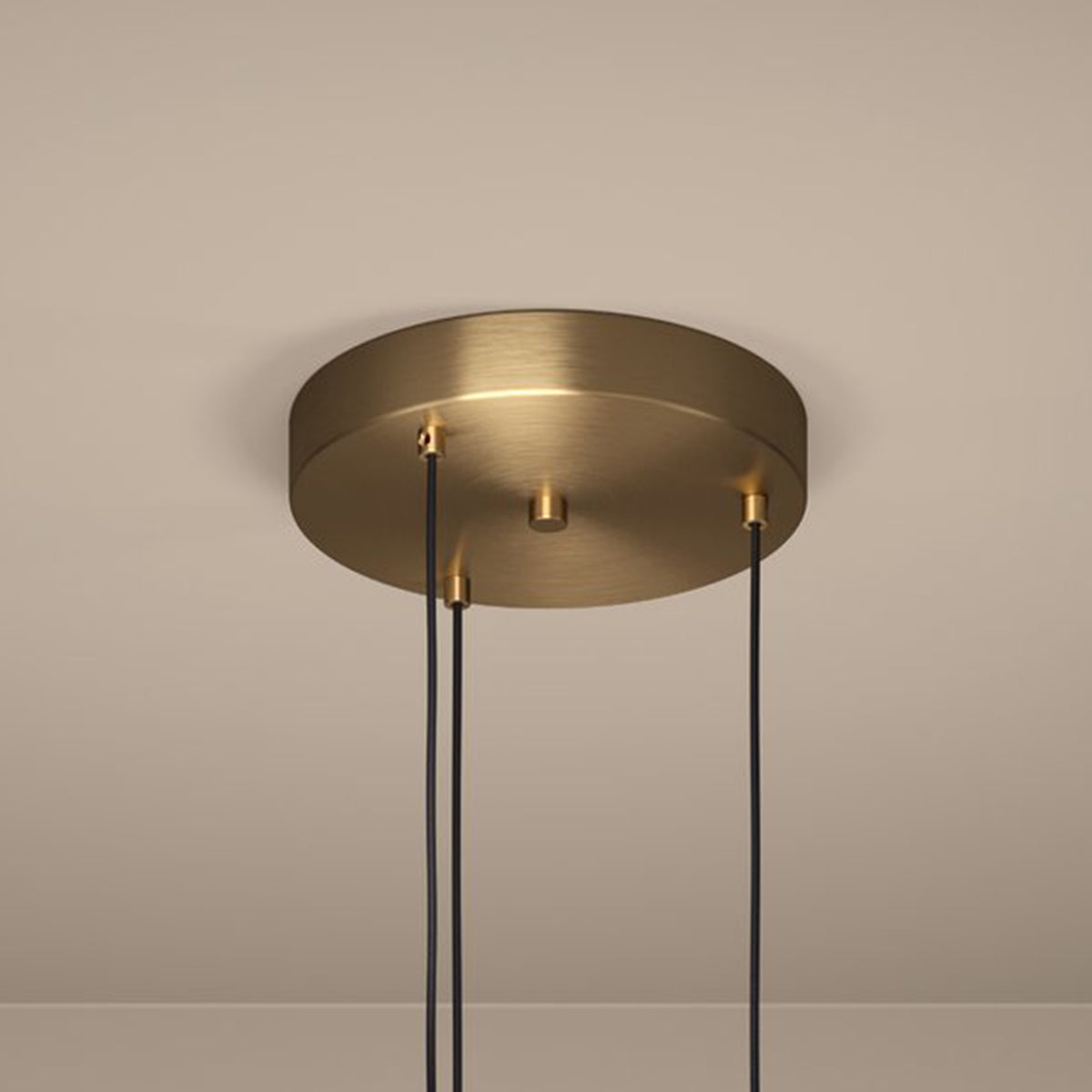 A close-up of a brass ceiling rose with three black cables hanging down, against a light beige ceiling.