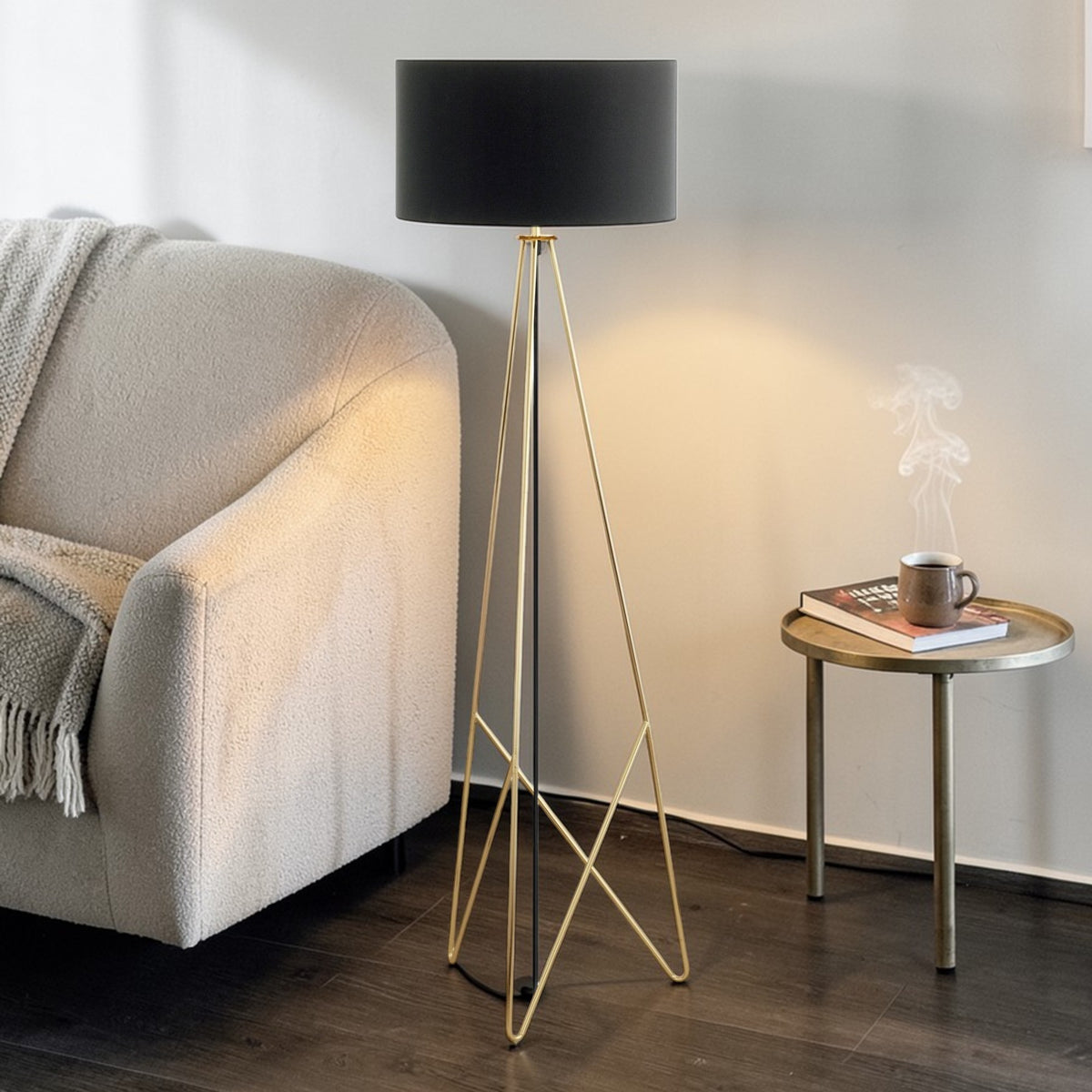 A black and gold floor lamp next to a cream sofa and a side table with a steaming mug.