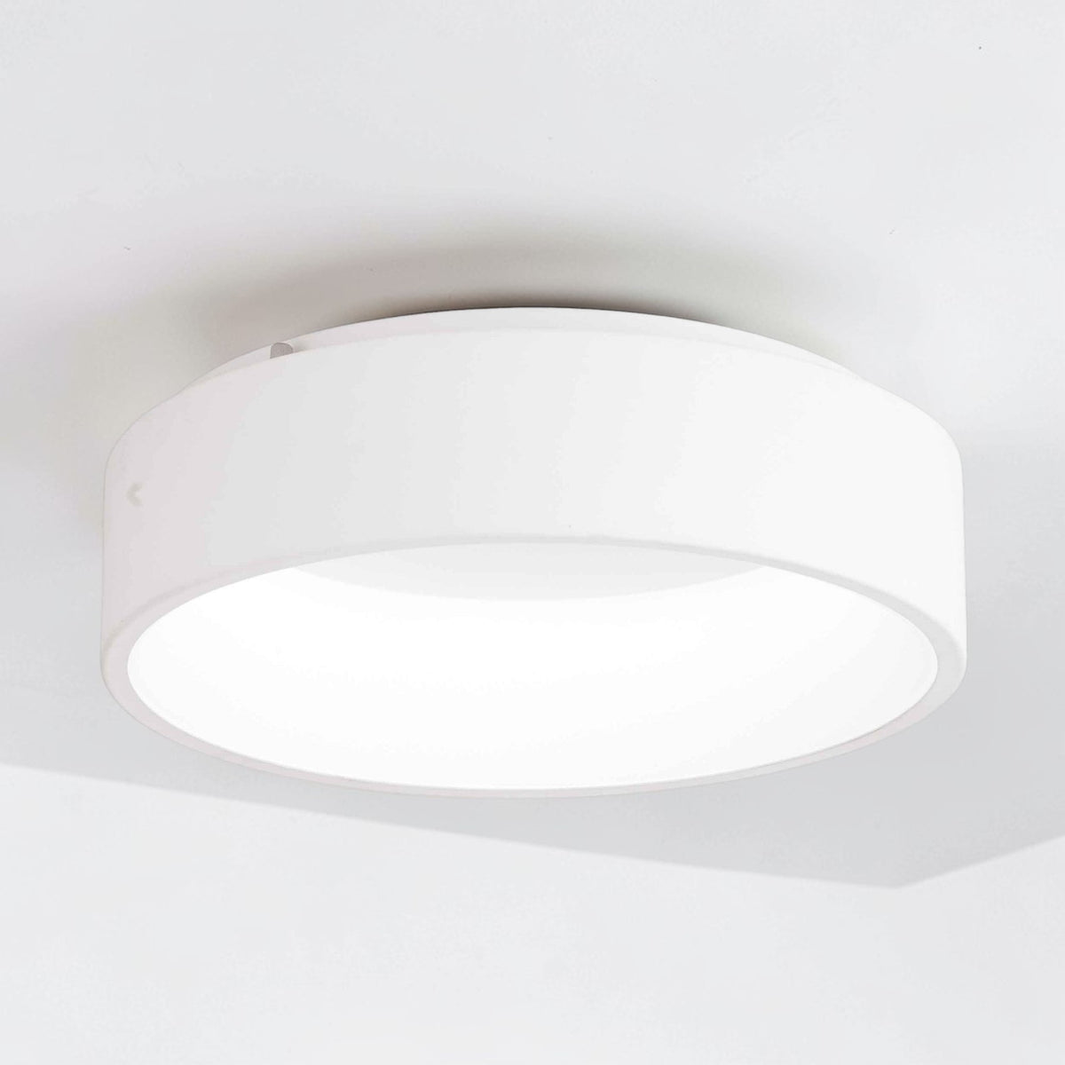 White round ceiling light fixture with a soft glow, mounted on a white ceiling.
