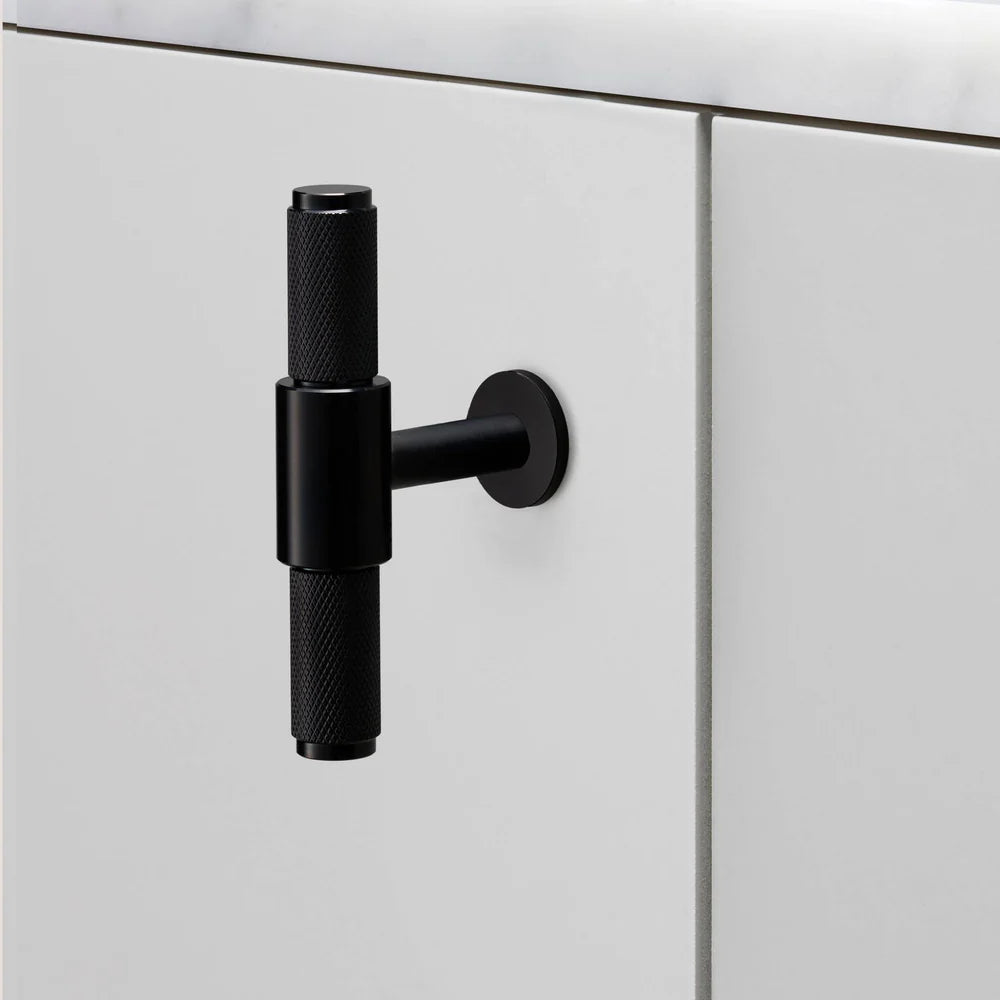 Black knurled T-bar handle on a white cabinet