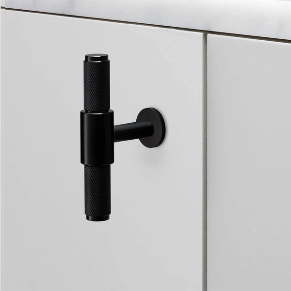 Black knurled T-bar handle on a white cabinet